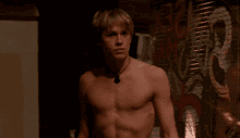 a shirtless man with a necklace around his neck stands in front of a painting of a guitar