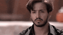 a man with a beard and earrings is looking at the camera .