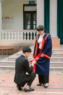 a man is helping a woman with her graduation gown in front of a building that has the number 103 on it