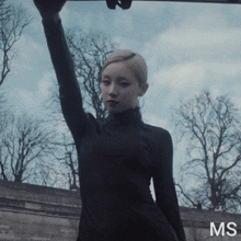 a woman in a black dress is standing in front of trees and the word ms is on the bottom right
