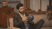 a man in a suit is sitting on a couch holding a ball