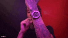 a man is smoking a cigarette in a dark room with purple lights behind him .