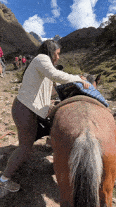 a woman pushes a brown horse on a dirt path