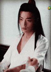 a man with long black hair and a white shirt is holding someone 's hand