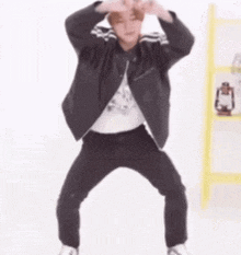 a man wearing a black jacket and black pants is dancing in a room .
