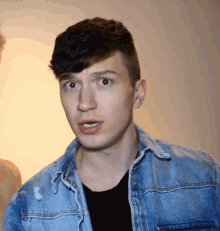 a young man wearing a denim jacket and black shirt looks surprised