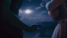 a woman in a white dress holds a man 's hand in front of a full moon