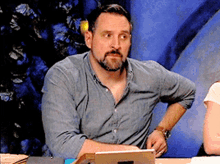 a man with a beard is sitting at a table with his hands on his hips