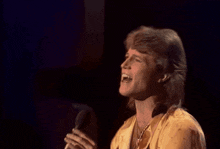 a man with long hair is wearing a yellow shirt and necklaces