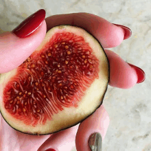 a person with red nails is holding a slice of fig