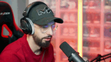 a man with a beard wearing headphones and a hat is talking into a microphone .