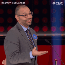a man in a suit and tie stands in front of a microphone with the words family feud canada on the bottom left