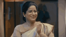 a woman in a white saree is smiling and clapping her hands in a room .