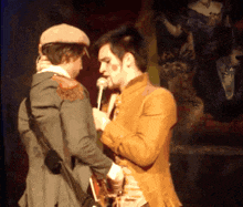 two men are standing next to each other and one is holding a guitar