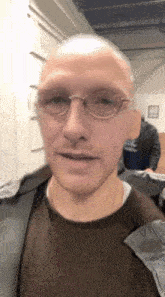 a close up of a man wearing glasses and a brown shirt