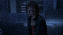 a woman in a black jacket stands in a dark room