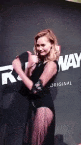 a woman in a black dress is standing in front of a wall that says runway original .