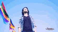 a man stands in front of a blue sky with rainbow flags behind him and the word toree on the bottom