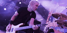 a man in a black shirt is playing a bass guitar on a stage