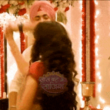 a man in a turban kisses a woman on the cheek in front of a sign that says saas bahu ke sajisha