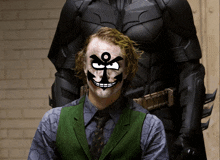 a man in a joker costume stands in front of a batman costume