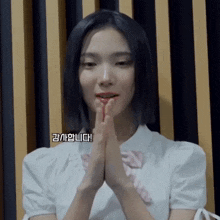 a girl in a white shirt has her hands folded in front of her mouth