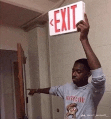 a man in a maryland shirt is holding up an exit sign over his head