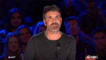 a man with a beard stands in front of a microphone with nbc written on the bottom of the screen