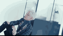 a man with white hair is sitting on the floor wearing a plaid jacket
