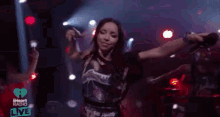 a woman is singing into a microphone on a stage at iheart radio live .