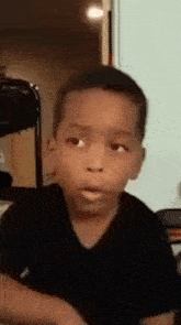 a young boy in a black shirt is making a funny face and looking at the camera .
