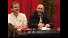 two men are sitting at a table and one of them is saying des barres j'ai juré des barres