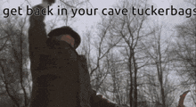 a man is standing in the woods with his arms in the air and a caption that says get back in your cave tuckerbags .