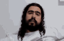 a man with long curly hair and a beard is wearing a white shirt that says until