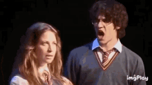 a man and a woman are standing next to each other on a stage . the man is wearing glasses .