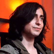 a man with long black hair wearing a green jacket