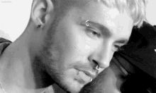 a black and white photo of a man with a nose ring and piercings .