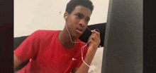 a young man wearing headphones and a red shirt is sitting in front of a computer screen .