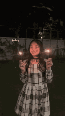 a girl in a plaid dress is holding sparklers and smiling