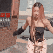 a woman wearing a black top and pink pants is standing in front of a brick wall with chinese writing on it