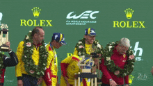 a group of men stand on a podium with rolex advertisements behind them