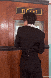 a man in a black suit stands in front of a ticket booth