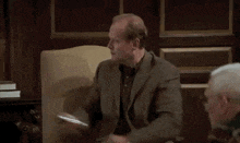 a man in a suit is sitting in a chair looking at a cell phone
