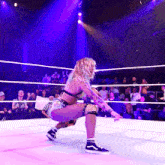 a woman is squatting in a wrestling ring with a crowd watching