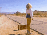 a woman walking down a dirt road holding a suitcase