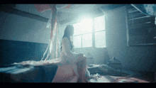 a woman in a white dress sits on a bed in a dark room