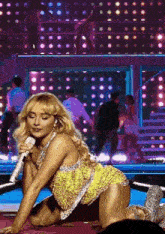a woman in a yellow dress is kneeling on the floor while holding a microphone on a stage .