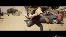 a man in a mask is running down a dirt road in front of a car .