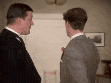 two men in suits are standing next to each other in a room and talking to each other .