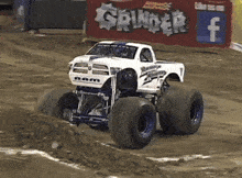 a white monster truck is driving on a dirt track in front of a sign that says grinder